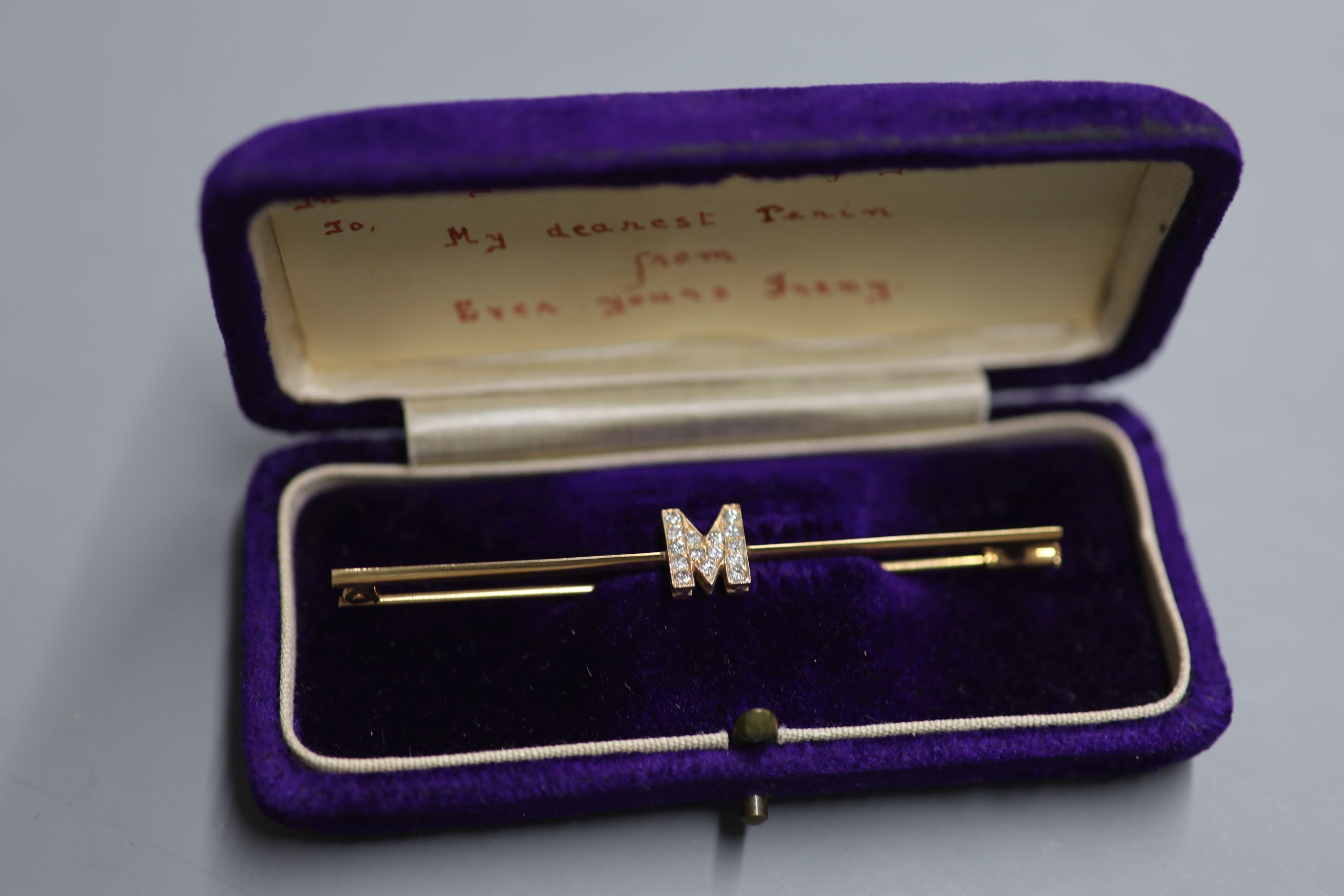 A yellow metal and diamond set initial M bar brooch, 77mm, gross 4.6 grams.